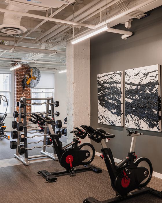 Modern fitness center featuring state-of-the-art exercise bikes, a comprehensive dumbbell rack, and contemporary artwork on exposed brick and concrete walls.
