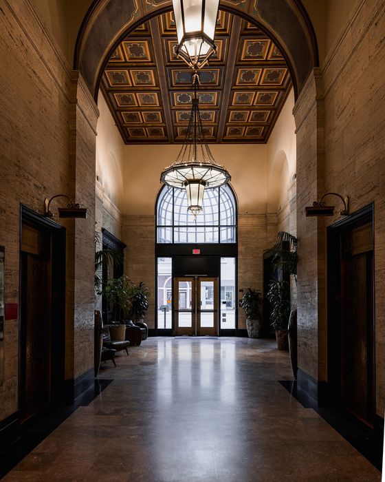 Elegant apartment lobby with towering ceilings, ornate chandeliers, and grand entrance doors, offering a luxurious ambiance.
