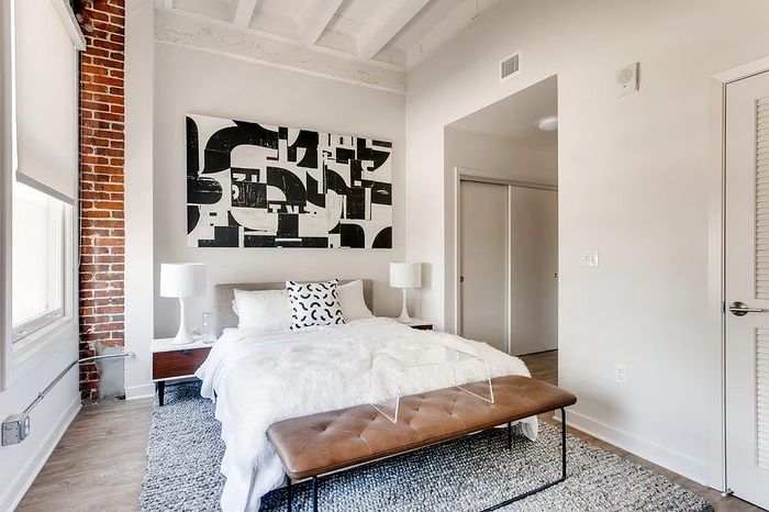 Chic urban bedroom with exposed brick wall, modern abstract art, and cozy decor, offering a stylish city living vibe.