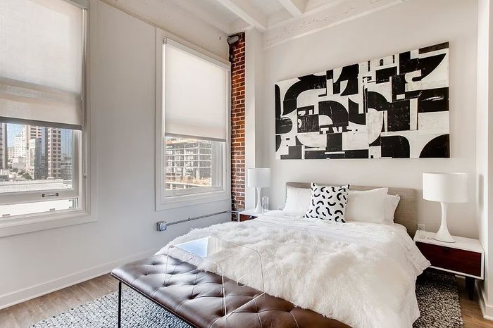 Bright and modern bedroom with large windows, contemporary art, and a plush bed in an urban setting.