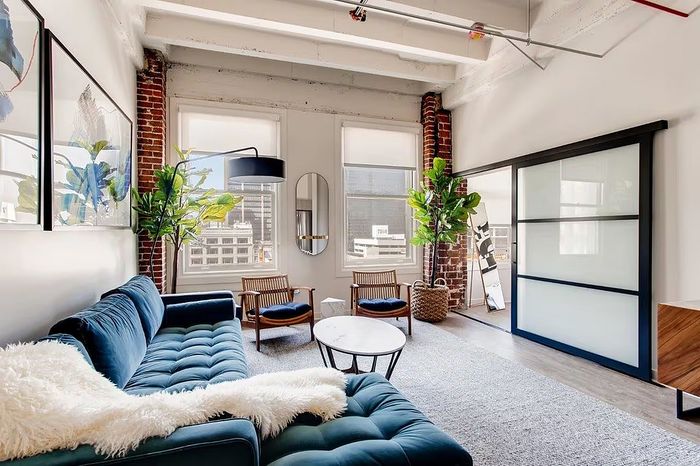 Chic urban living room with industrial charm, featuring a plush blue sofa, stylish wall art, and abundant natural light.