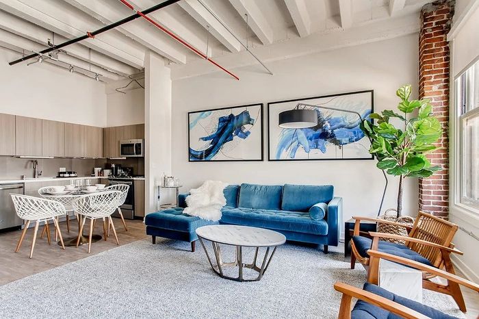 Contemporary living space with bright open kitchen, stylish blue sofa, modern art, and cozy dining area designed for comfort and elegance.