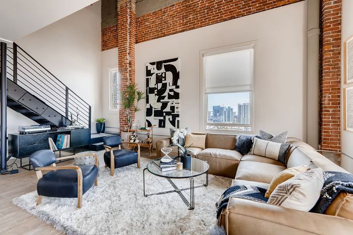 Chic urban loft with exposed brick, modern decor, and a cozy sectional sofa in a sunlit living space overlooking city views.