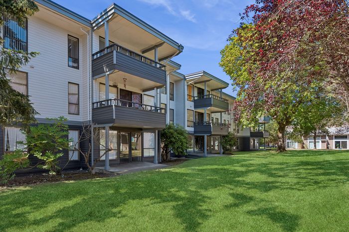 Charming apartment complex with spacious balconies set against a vibrant, green lawn and lush trees.