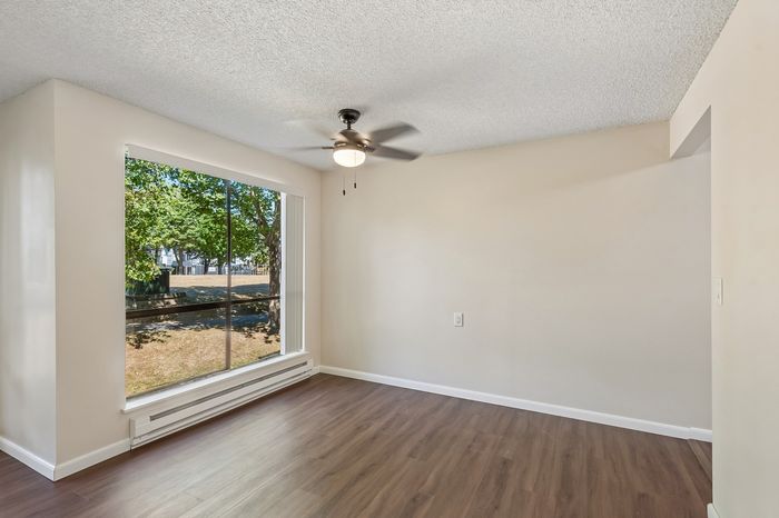 Bright and airy room with elegant wood flooring, large window with scenic outdoor view, and modern ceiling fan.