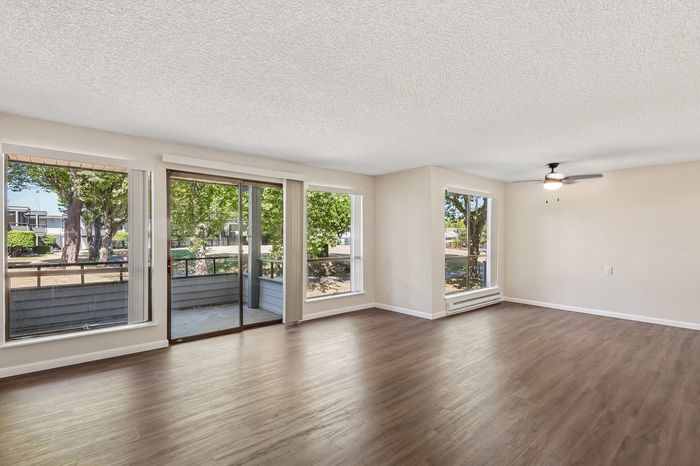 Bright and airy living room with large windows, modern ceiling fan, and sleek wood flooring offering stunning natural views.