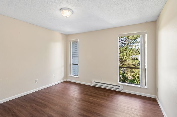 Bright bedroom with elegant wood flooring and large windows overlooking lush greenery.