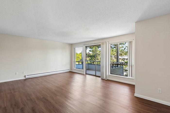 Bright and airy living room with elegant wood flooring, large windows offering lush green views, and ample natural light.