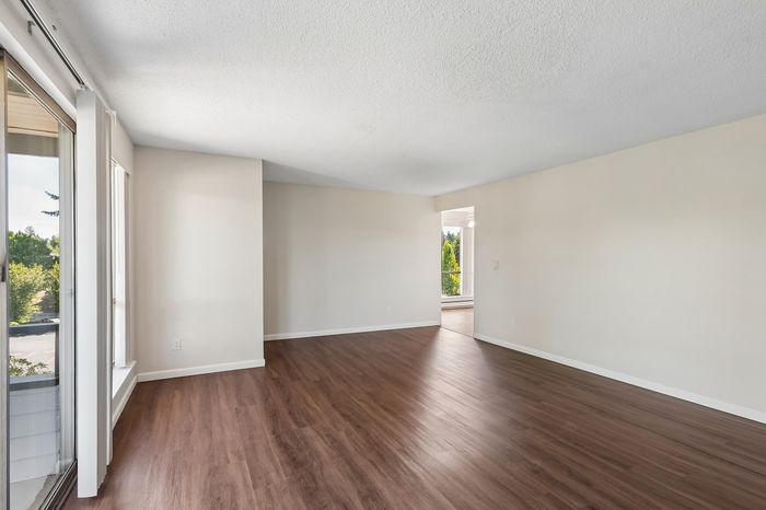 Bright and spacious living room with elegant wood flooring and large windows offering lush green views.