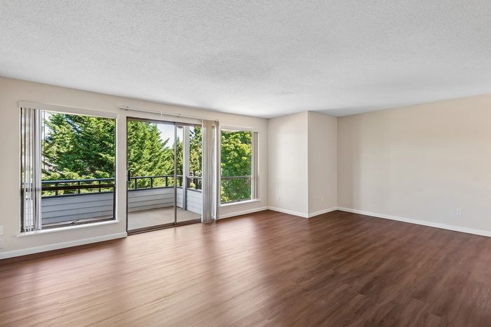 Bright and airy apartment living room with large windows, warm hardwood floors, and lush green views creating a serene atmosphere.