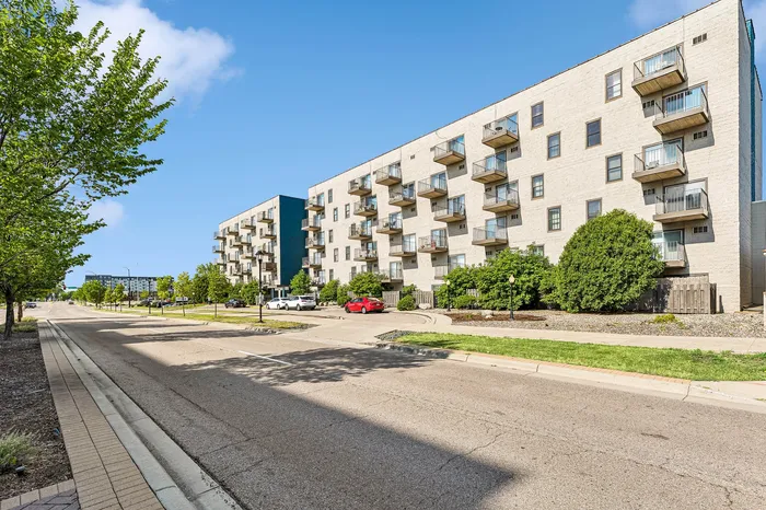 Charming apartment complex with modern balconies, surrounded by lush greenery and set against a clear blue sky.