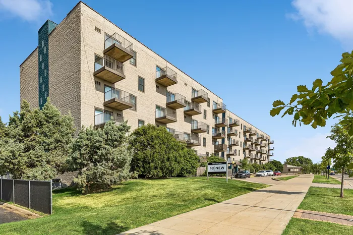 Chic apartment building with modern balconies, surrounded by lush greenery and a clear blue sky, offering a refreshing urban living experience.