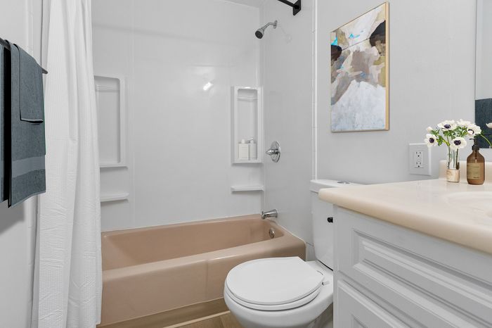 Elegant modern bathroom featuring a chic beige bathtub, white vanity with fresh flowers, and sleek minimalist decor.
