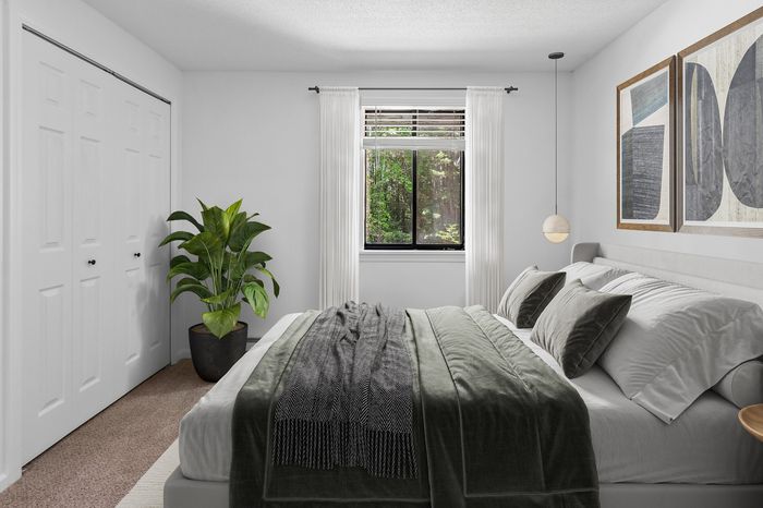 Elegant bedroom with plush bedding, modern art, and a lush green view through the window, creating a serene ambiance.