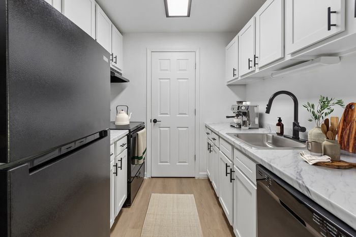Modern galley kitchen with sleek black appliances, white cabinetry, and elegant marble countertops.