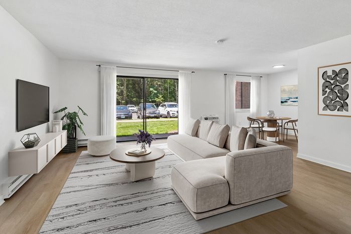 Bright and modern living room with sleek furniture, large windows, and elegant decor, offering a serene view of lush greenery outside.