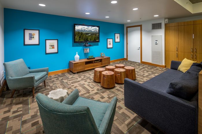 Chic modern lounge with vibrant blue wall, cozy teal chairs, sleek wooden accents, and a wall-mounted TV for perfect relaxation.