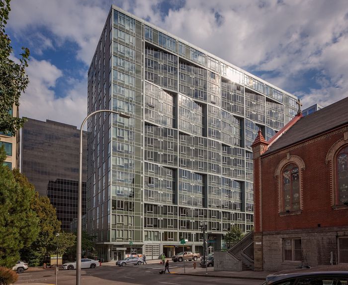 Contemporary high-rise apartment building with sleek glass facade, situated in a vibrant urban area with historic architecture nearby.