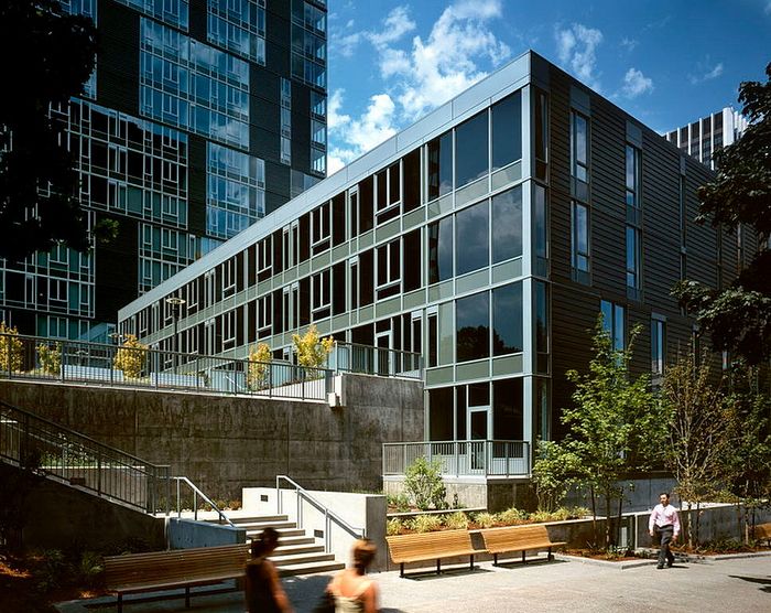 Modern urban apartment complex with sleek glass facade, surrounded by lush greenery and open communal spaces.