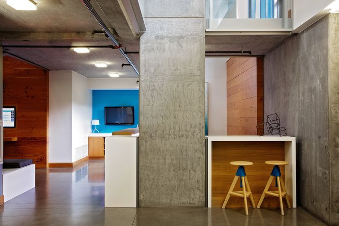 Modern apartment interior featuring a stylish bar area with wooden stools, vibrant blue accent walls, and a sleek concrete column.