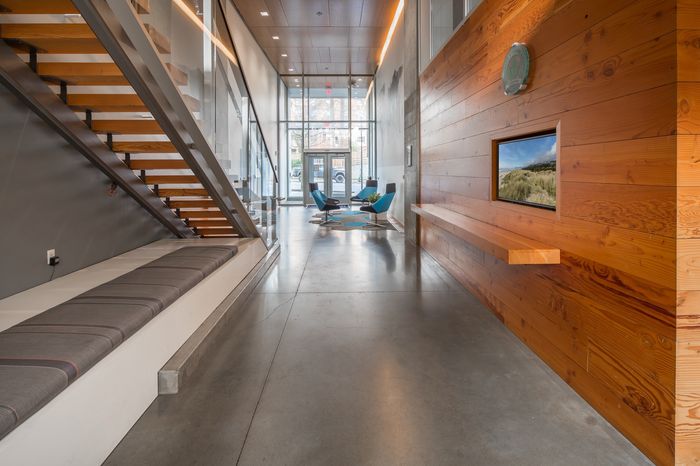 Modern apartment lobby with sleek metal staircase, cozy seating area, and warm wooden accents, bathed in natural light.
