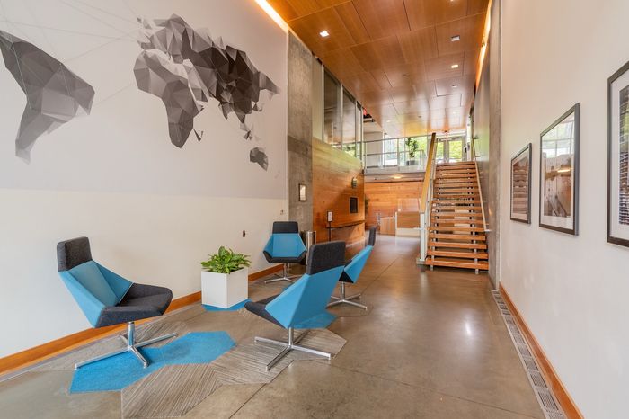 Modern lobby area with contemporary blue chairs, geometric wall art, and wooden staircase, showcasing an inviting and stylish space.