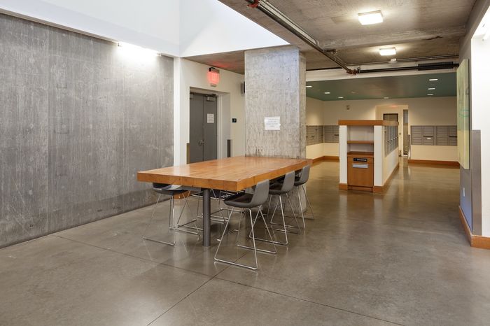 Modern apartment corridor with sleek concrete walls and an inviting wooden table, complemented by contemporary seating for social gatherings.