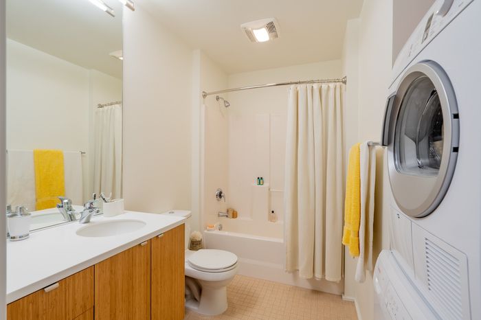 Bright and modern bathroom with sleek cabinetry, a shower-tub combo, and in-unit washer and dryer for convenient living.