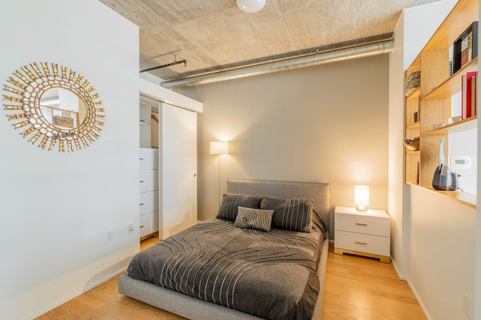 Modern bedroom with sleek gray bedding, stylish wall mirror, and wooden shelves, exuding a cozy and contemporary vibe.