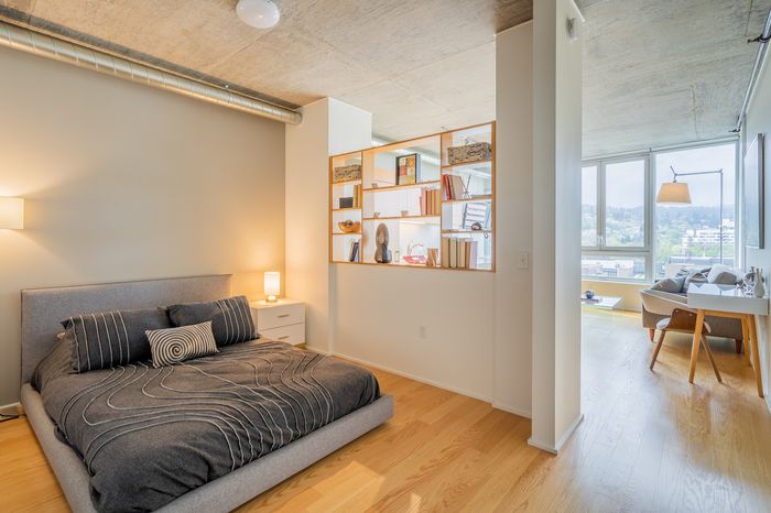 Chic urban bedroom with modern decor, stylish shelving, and bright natural light from large windows overlooking a scenic view.