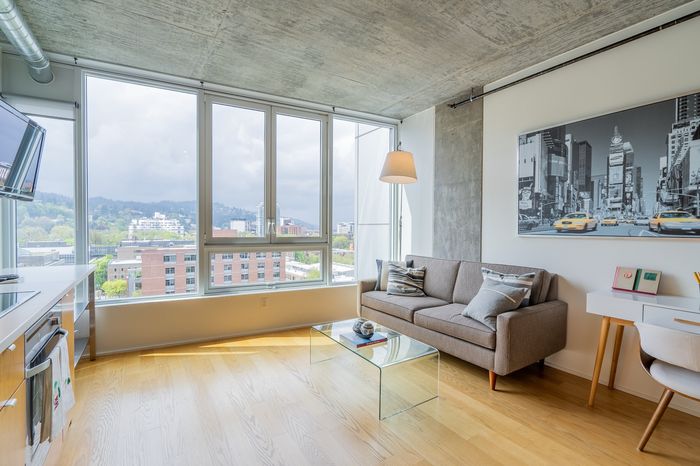 Chic urban living room with expansive window views, sleek gray sofa, glass coffee table, and vibrant cityscape artwork.