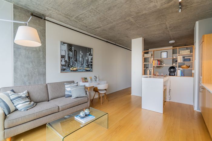 Modern apartment living room with sleek lighting, cozy gray sofa, artistic cityscape wall art, and a functional home office nook.