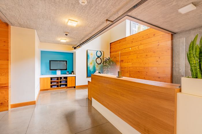 Modern lobby area featuring elegant wooden reception desk, vibrant artwork, and a cozy waiting nook with TV.