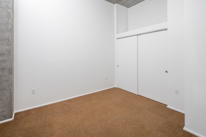 Minimalist room with warm carpet flooring, sleek white walls, and built-in closet doors, offering a versatile space for customization.