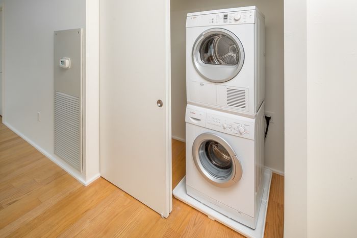 Convenient in-unit stacked washer and dryer tucked in a sleek, white closet, offering modern laundry amenities on warm wooden floors.