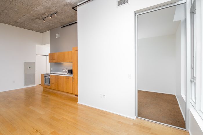 Contemporary open-plan apartment featuring a sleek kitchen with modern wooden cabinets and bright, spacious living area with hardwood flooring.