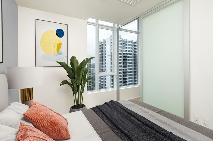 Modern bedroom with large windows offering a stunning city view, featuring stylish decor and vibrant artwork.