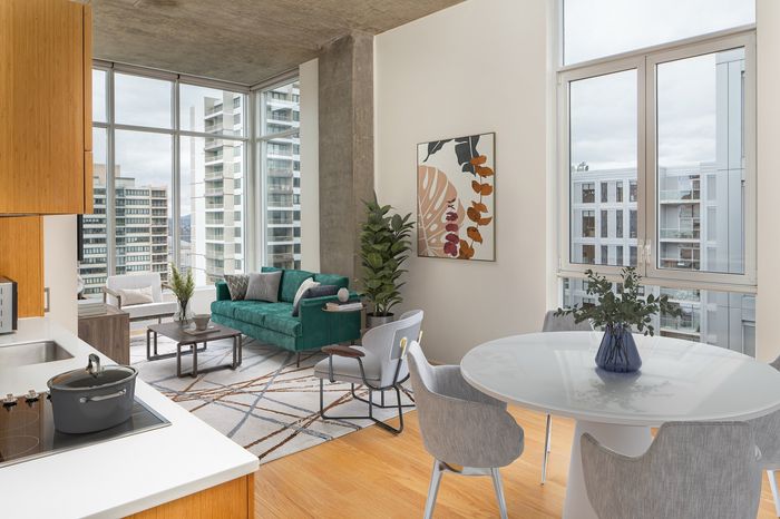 Modern open-concept apartment featuring a cozy living area with a green sofa, large windows offering stunning city views, and a stylish kitchen with sleek fixtures.