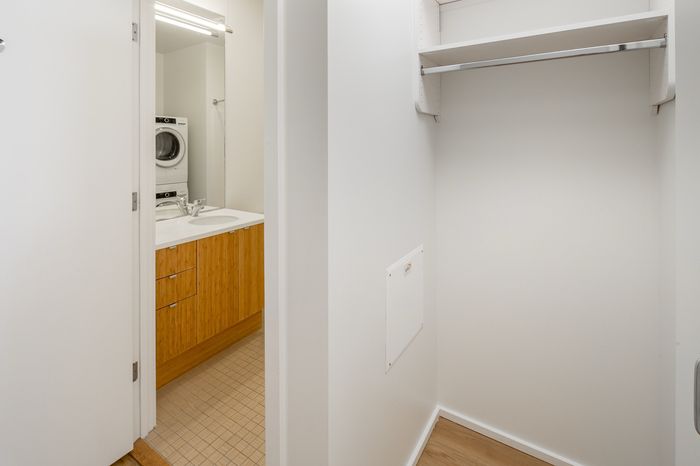 Modern bathroom with sleek wooden cabinetry, in-unit washer and dryer, adjacent to a spacious walk-in closet.