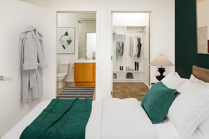Elegant bedroom with a luxurious green-accented bed, featuring an open walk-in closet and a stylish ensuite bathroom.