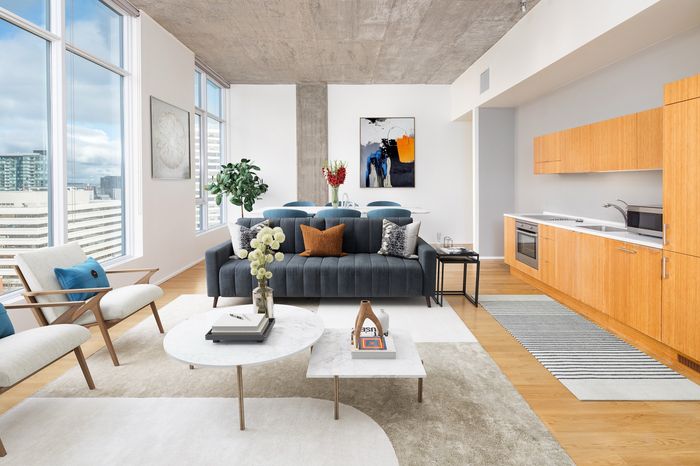 Modern open-concept living space featuring a chic cozy lounge area, full-height windows with city views, and a sleek linear kitchen with warm wooden cabinetry.