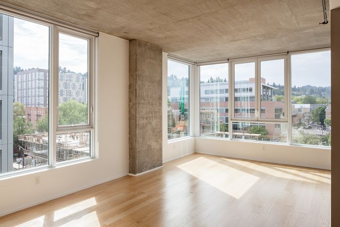 Modern apartment interior featuring large corner windows with stunning cityscape and natural light, showcasing chic concrete and wood accents.