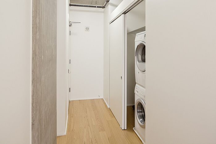 Modern apartment hallway featuring a convenient in-unit washer and dryer set, offering style and practicality with sleek white walls and hardwood flooring.