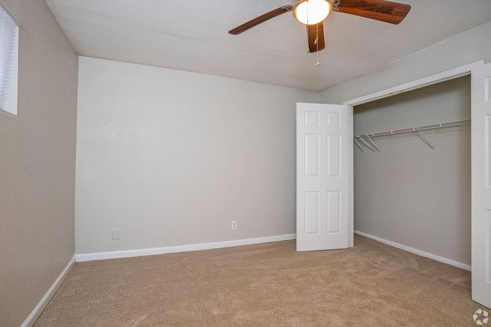 Inviting bedroom with plush carpet, ceiling fan, and ample closet space in a modern apartment.