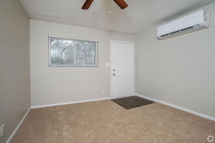 Bright and cozy room with plush carpet, large window, and modern air conditioning unit.