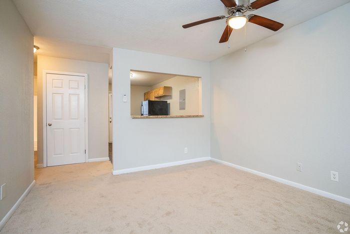 Cozy living room with plush carpet and modern ceiling fan, adjacent to an open kitchen with a breakfast bar.
