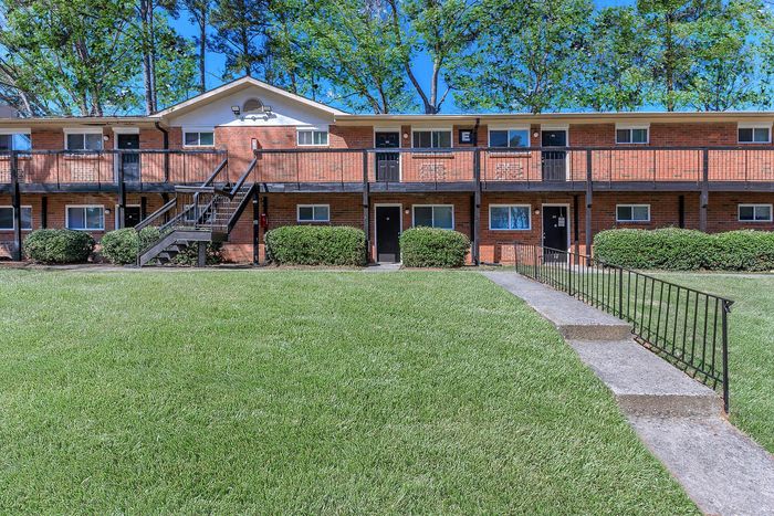 Charming brick apartment complex with lush green landscaping and a welcoming front entrance.