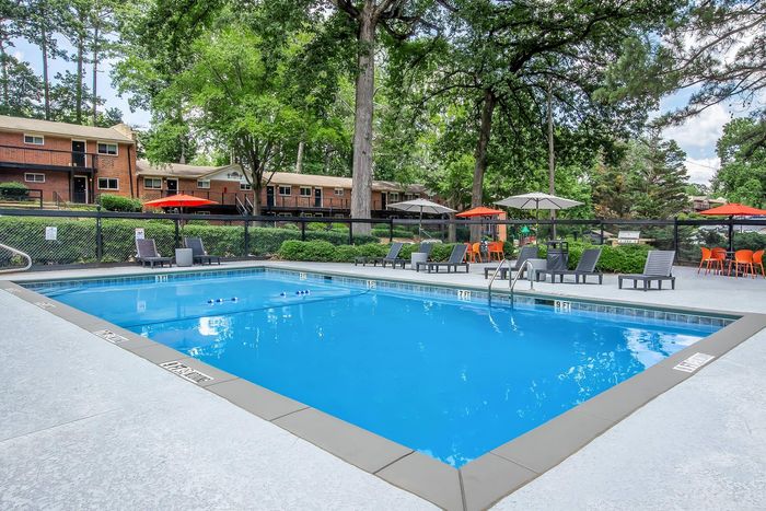 Inviting outdoor pool area with sleek lounge chairs and vibrant umbrellas, set amidst lush greenery for a relaxing retreat.