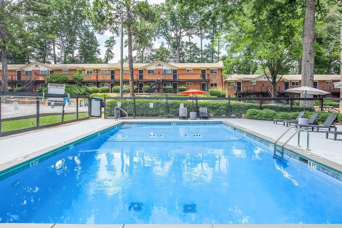 Inviting outdoor pool surrounded by lush greenery and stylish loungers, offering a serene retreat at a charming apartment complex.