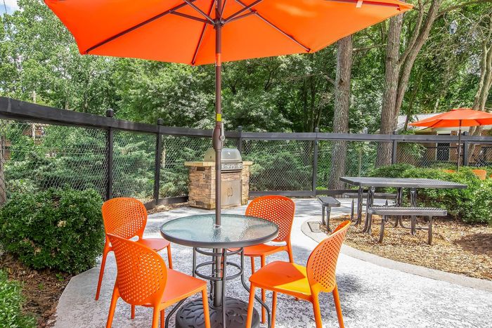 Inviting outdoor space featuring bright orange chairs and umbrellas, perfect for relaxation and barbecues in a lush green setting.